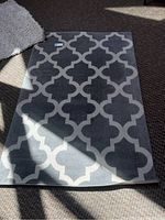 Full view of rectangular grey and off-white patterned area rug laid on carpeted floor with sunlight shadow