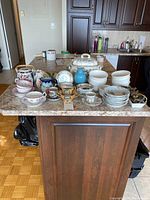 Full view of assorted porcelain and china items arranged on kitchen counter, including stack of plates, cups, bowls, and the soup tureen set with lid, ladle, and tray.