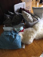 Photo showing assorted decorative pillows in various fabrics and colors, cream faux fur throw, and a blue comforter on the floor.