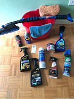 Full lot of car cleaning supplies including bucket, brushes, sponge, cloth, and several bottles of cleaners and wax sprays.