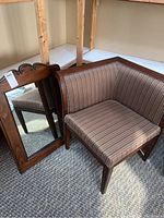Photo showing an upholstered corner chair with striped fabric cushion and wooden frame beside a wood-framed wall mirror with carved detailing at top.