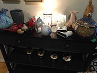Wide photo showing the mix of decor items on a black table including vases, figurines, candle holders, and musical snow globes below the table.