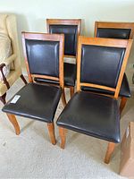 Four wooden dining chairs with black upholstery shown together in a room setting.