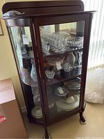 Full view of the wood and glass display cabinet with curved sides and glass door, showing various glassware inside (not included in sale).