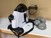 Under desk exercise pedal bike with adjustable knob and pedal straps on a white surface with two 8 lb dumbbells nearby
