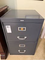 Front view of gray metal 2 drawer filing cabinet with two white handles and label holders, sticker and lot number tag visible.