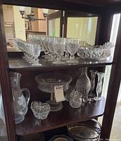 Shelf displaying multiple cut glass and crystal items, including a pitcher, bowls, decanter, and silver plate items.