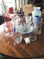 Photo shows a collection of 9 glass items including pitchers, vases, bowls, and drinking glasses placed on a wooden table.