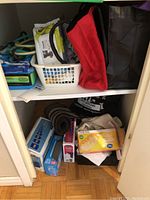 Shelving with boxes of garbage bags, reusable fabric bags in red and black, white basket with pet wipes and cloths, smaller miscellaneous cleaning supplies on lower shelf.