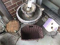 Photo showing the outdoor solar garden fountain, two metal garden pot stands, a small birdhouse, and a wicker basket grouped together.