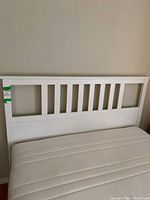 Front view of white IKEA bed headboard with vertical slats and the queen foam mattress on the frame