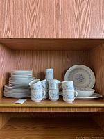 Photo showing the stacked plates, cups, and saucers with the distinctive blue Galaxy pattern on white china, arranged on a wooden shelf.