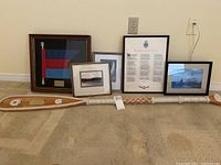 Wide view showing all items in the lot including framed paintings, poem, flag, and oar on carpeted floor against baseboard