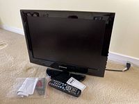 Samsung 19-inch television with remote control, power cord, and user manual on beige carpet.