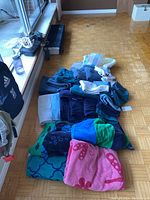 View of a large assortment of towels in various colors and patterns laid out on the floor, showing pink towel with paw prints, blue and green patterned towels, and multiple solid-colored towels in shades of blue, green, and teal.