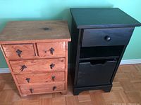 Two small dresser tables side by side, one natural wood with 6 drawers and metal handles, one black table with a single drawer, open shelf, and removable wooden storage box.