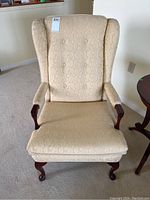 Front view of the wing back chair showing floral upholstery, tufted backrest, and wooden legs