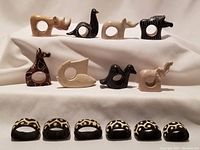 Full lot of 14 carved napkin rings displayed on white fabric background. Includes animal and bird shapes in various natural stone colors.
