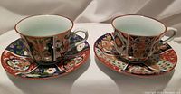 Front view of the two Japanese Imari porcelain teacups and matching saucers showing colorful hand-painted floral and geometric designs in red, blue, green, and gold.
