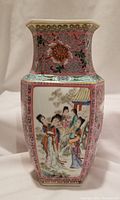 Front view of hexagonal porcelain vase showing a painted scene with Chinese ladies in traditional attire surrounded by floral and scroll patterns on a pink ground.