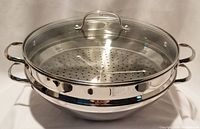 Full assembled view of stainless steel steamer insert sitting atop wok bowl with glass lid on top.