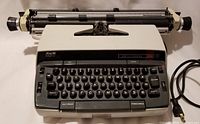 Front angled view of off-white and gray Smith Corona 250 electric typewriter showing keyboard, carriage and power cord.