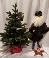 Father Christmas figure standing next to artificial pine tree in red ceramic pot, and wooden star on floor