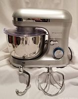 Front view of silver Frigidaire stand mixer with stainless steel bowl and two metal attachments in front (dough hook and flat beater).