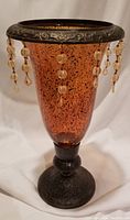 Full view of the amber glass vase with metal rim decorated with hanging glass bead tassels.
