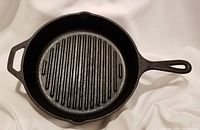 Full top view of the black Lodge cast iron grill pan showing circular shape, grilling ridges, long handle and helper handle.