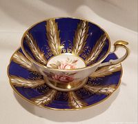 Close-up view of teacup inside showing interior design of pink rose and gold feather pattern on cobalt blue background and the cup's gold handle.