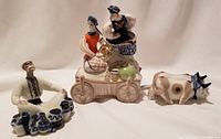 Set of three porcelain Ukrainian village figurines including a cart with seated man and woman and an ox figurine.