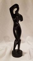 Front view of a black abstract female figure sculpture in a standing pose with raised arm and circular cutout.