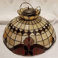 Full view of Tiffany-style stained glass shade showing decorative geometric and floral motifs in cream, brown, red, and orange glass pieces with top metal hanging loop.