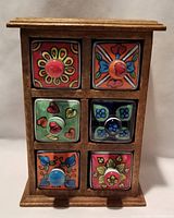 Front view of wood cabinet with six colorful handpainted ceramic drawers, each with a round knob.