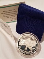 Medallion in clear plastic capsule, navy felt holder embossed with trident emblem and folded certificate behind
