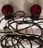 Photo of two round magnetic tow lights with red lenses, black housing, and tangled cables, showing the full set and wiring.