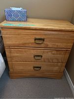 Wooden dresser showing three drawers and metal handles, wood grain visible, placed against a wall.