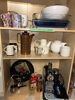 Full shelf view showing Nespresso machine, stove-top coffee pot, various mugs, glass baking dishes, and other vessels.
