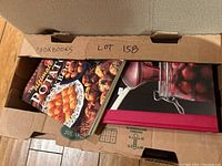 Two small boxes filled with assorted cookbooks and recipe collections, showing titles like 'Ultimate Potato Cookbook' and an image of cherries in a glass jar.