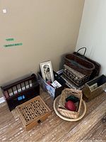 Photo showing multiple decorative items including magazine racks, baskets, maze game, a wooden and metal box, a woven bowl, and other containers grouped in a room corner.