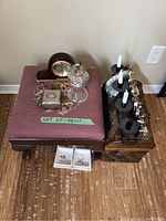 Photo of footstool top with clock, oil lamp, metal box, candle holder, and the two ceramic dishes on floor nearby.