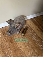 Photo showing a carved wooden pig figurine and a brass dog figurine on a wooden floor next to a wall baseboard.