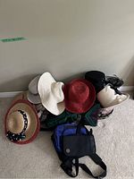 Side angle of various hats stacked on top of bags on a carpeted floor showing assortment and colors