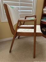 Side view of wooden chair showing boomerang shaped armrest and angled legs in natural wood finish.