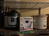 Shelf showing Instant Pot IP-Lux, Handy Gourmet MicroMaster microwave pressure cooker in box, and Rival crockpot slow cooker.