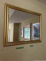 Front view of rectangular beveled glass mirror with gold painted frame reflecting framed wall art