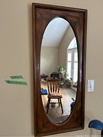 Frontal photo showing full wooden framed oval mirror in an interior setting with some furniture reflected.