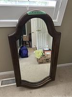 Mirror with wooden frame hanging on wall, showing curved top and bottom with dark finish, approximately 24x12 inches.