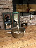 Overview of two rustic rectangular mirrors leaning against a stone wall, two lamps including one with a black adjustable arm, a brass bucket, and a metal bucket on wooden floor.